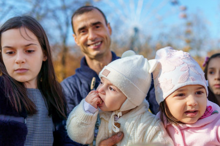 family has picnic in autumn city park, father and daughters, children and parent sitting together at the table, with apples and yellow maple leaves, happy people enjoying beautiful natureの写真素材