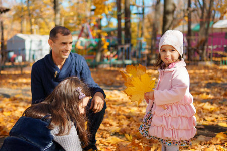 portrait of a family with children in an autumn city park, happy people walking together, playing with yellow leaves, beautiful nature, bright sunny dayの写真素材