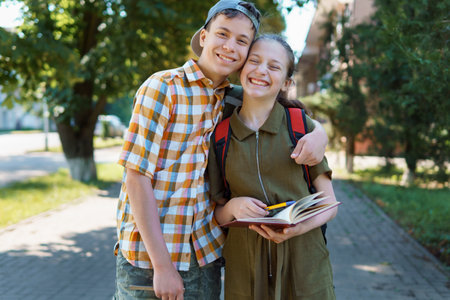 school students, a teenage boy and a girl are walking down the street, having fun, talking, reading books, a bright summer day in a city parkの写真素材