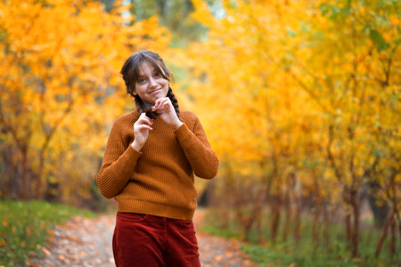 a young teenage girl poses in an autumn forest, enjoying the beautiful nature and bright yellow leavesの写真素材