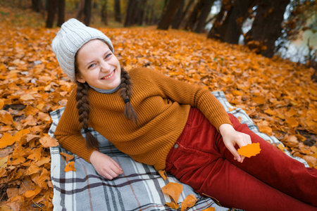 a young teenage girl is lying in a glade in the autumn forest, enjoying the beautiful nature and bright yellow leavesの写真素材