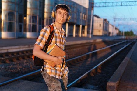 a student poses at a railway station, a teenage boy walks along the platform to the train, he has a backpack and books, goes to study, the concept of educationの写真素材
