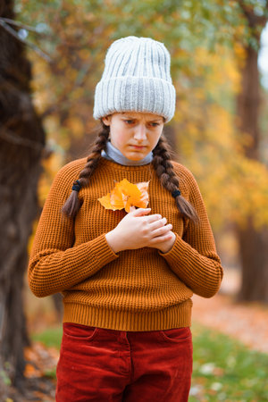 a young teenage girl posing in an autumn forest, she is unhappy and has a sad mood, standing by a tree, beautiful nature and bright yellow leavesの写真素材