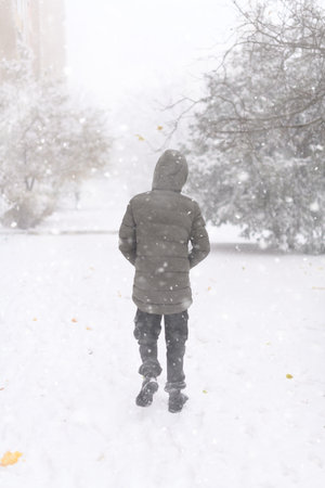 A boy walks along a snowy street, it is snowing, blizzard and frost on a winter dayの写真素材