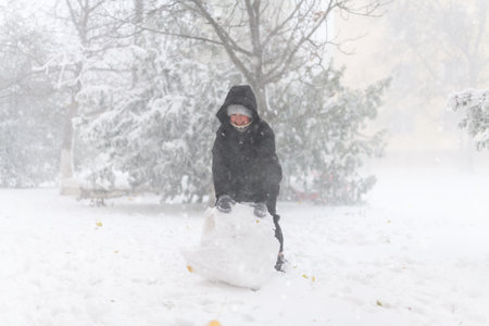 a girl is playing with snow on the street, it is snowing, a blizzard and frost on a winter day