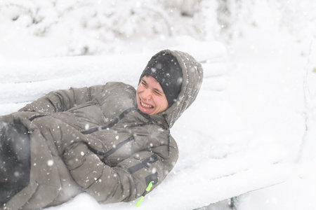 a boy lies in the snow on a bench, on a snowy street, it is snowing, a blizzard and frost on a winter dayの写真素材