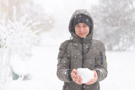 a boy is playing with snow on the street, it is snowing, a blizzard and frost on a winter dayの写真素材