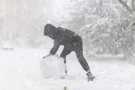 a girl is playing with snow on the street, it is snowing, a blizzard and frost on a winter dayの写真素材