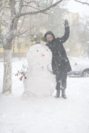 a girl is playing with snow on the street, making snowman, it is snowing, a blizzard and frost on a winter dayの写真素材