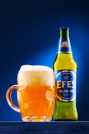 Tiraspol, Moldova - March 18, 2024: A bottle of Efes Pilsener beer and a full glass poured on a dark blue backdrop. The beer foams up and bubbles.のeditorial素材