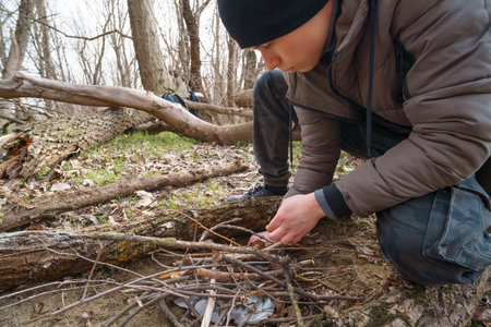 A teenage boy makes a bonfire in the forest, while hiking and outdoor activities, early spring...