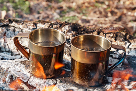 two iron mugs with boiling water for tea over a campfire, cooking while hikingの写真素材
