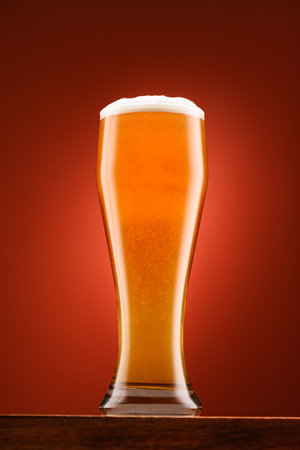 glass of beer, on wooden stand, with red background, object close-up, beer bubbles and foamの写真素材