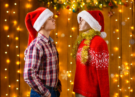 A teenage boy poses with a male mannequin as a friend in New Year decorations with festive illumination and garlands, Christmas lights and decorations, Holiday themeの写真素材