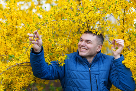 portrait of a man on the background of yellow forsythia flowers, spring nature and blossoms