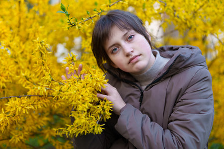 portrait of a girl on the background of yellow forsythia flowers, spring nature and blossomsの写真素材