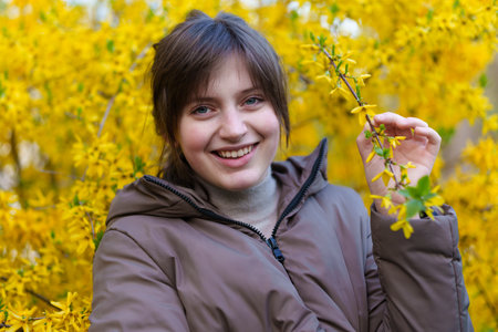 portrait of a girl on the background of yellow forsythia flowers, spring nature and blossomsの写真素材