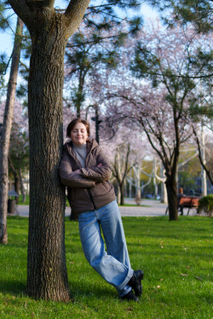 portrait of a teenage girl in a spring park, stands leaning against a treeの写真素材