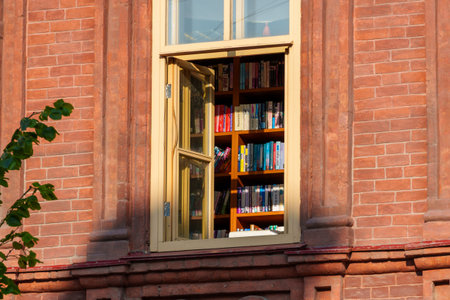 An open library window, bookshelves, a red brick building facadeの写真素材
