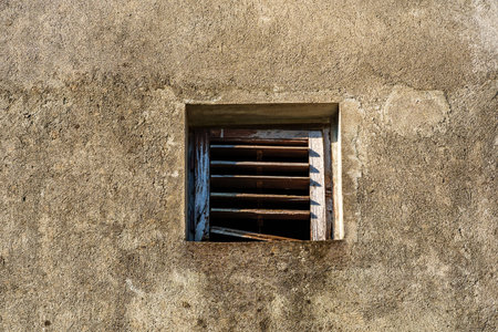 old weathered plaster wall with small ventilation window with wooden blindsの写真素材