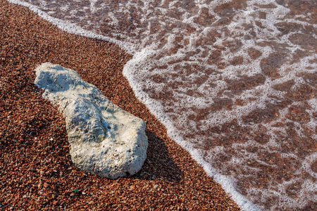 big beautiful white stone lies on coastline and small stones of beach of Adriatic Sea, with beautiful foaming wave, as abstract background of summer travel and vacationの写真素材