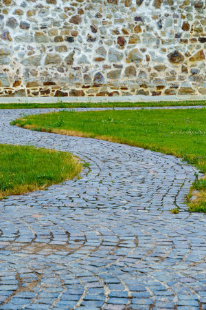 old stone wall of ancient monastery and cobblestone pavement, green lawn, beautiful landscapeの写真素材
