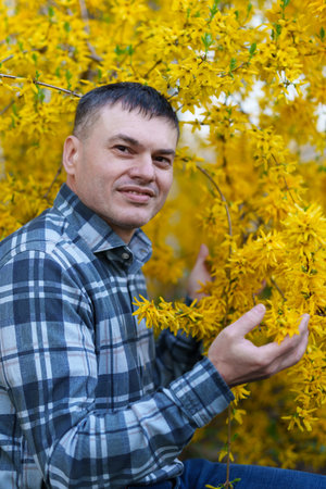 portrait of a man on the background of yellow forsythia flowers, spring nature and blossomsの写真素材