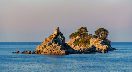 A beautiful seascape at dawn overlooking the sea and an island with a small church on top of a cliff. Sveta Nedelya and Katic Islands, Petrovac city, Montenegroの写真素材
