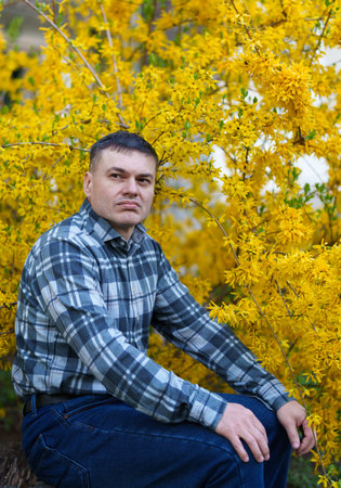 portrait of a man on the background of yellow forsythia flowers, spring nature and blossomsの写真素材