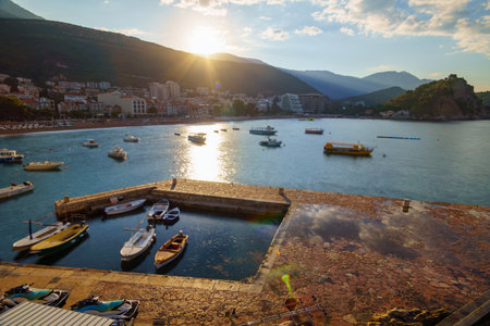 seascape and panorama of a resort town with a beach, hotels and boats, Petrovac, Montenegro, mountains and sunlightの写真素材