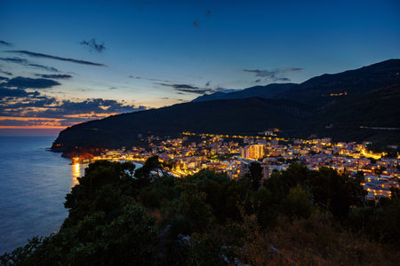 sunset in small resort town Petrovac, Montenegro, beautiful sea view, city embankment with street lights, beach and mountains against sunset skyの写真素材