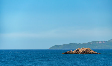 view of a small island far out at sea, rocks, trees, blue sky, water and waves, summer vacation travel conceptの写真素材