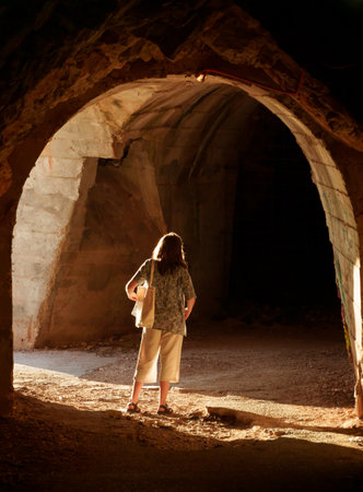 A girl poses in a tunnel, the beautiful sunset sunlight creates long shadows on the arch and wallsの写真素材