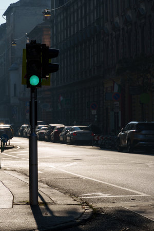 A high-contrast urban scene of bright sunlight and shadows cast by buildings at a road intersection with a traffic light, city streets view, architecture and trafficの写真素材