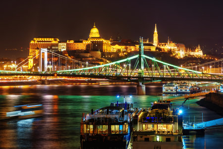 Panoramic view of Budapest city and the Danube River at night, Liberty Bridge, tour boats, urban architecture with beautiful illumination, street lights and road trafficの写真素材