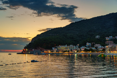 sunset in small resort town Petrovac, Montenegro, beautiful sea view, city embankment with street lights, beach and mountains against sunset skyの写真素材