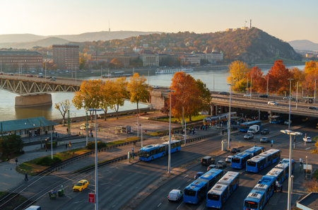 Panoramic view of Budapest and the Danube River at sunset, city architecture, bridges, and road traffic. Trees with yellow autumn leaves and a view of Gellert Hill.の写真素材