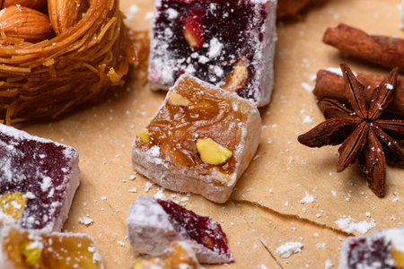 Extreme close-up of a traditional middle eastern dessert: a crunchy kataifi nest filled with whole almonds, surrounded by various cubes of turkish delight (lokum) with powdered sugarの写真素材