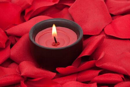 Candle surrounded with red rose petalsの写真素材