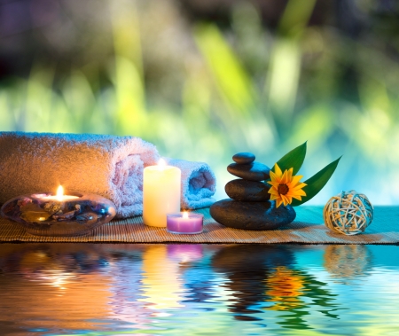 three candles and towels black stones and orange daisy on waterの写真素材