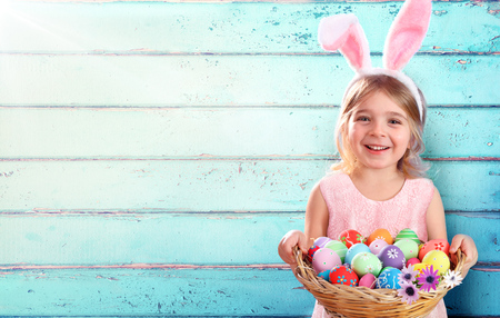 Easter - Little Girl With Basketball Eggs And Bunny Ears And Blue Wooden Backgroundの写真素材