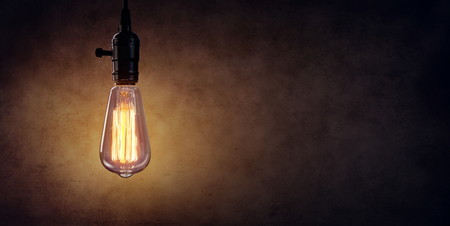 Vintage Hanging Light Bulb Over Dark Wallの写真素材