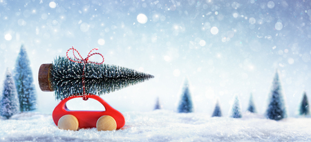 Red Car Carrying A Christmas Tree In Snowy Forestの写真素材