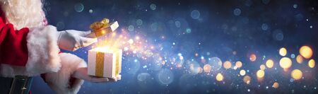 Santa Claus Opening Christmas Present With Golden Stars In Nightの写真素材