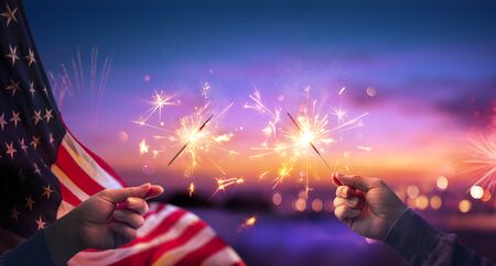 Use Celebration With Hands Holding Sparklers And American Flag At Sunset With Fireworksの写真素材