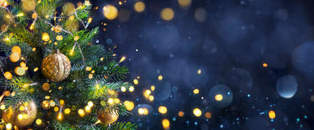 Christmas Tree In Blue Night - Golden Balls On Fir Branches With Defocused Lights In Abstract Backgroundの写真素材