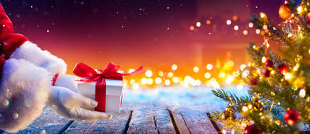 Santa Claus Putting Gift Present Below Christmas Tree With Abstract Lights At Nightの写真素材
