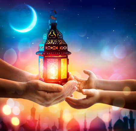 Muslim Holy Month Ramadan Kareem - Hand Give To Kid Arabic Lantern Glowing At Evening With Abstract Defocused Lights - Eid Ul Fitrの写真素材