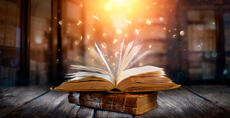 Old Book With Magic Lights And Bright Letters On Aged Table In Defocused Libraryの写真素材