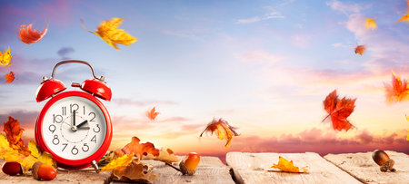 Fall Back Time - Daylight Savings End - Clock Alarm At Sunrise With Leaves - Return To Winter Timeの写真素材